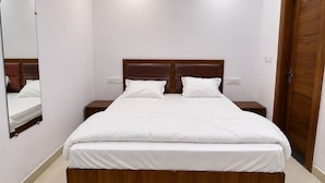 Quarto com uma cama grande, cabeceira de madeira, duas mesas de cabeceira, um espelho e uma porta de madeira.