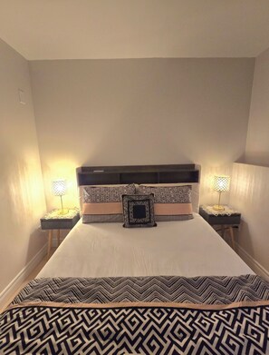 A neatly made bed with patterned bedding, two bedside tables with lamps, and a headboard with a geometric design. - Comfy 5 bedroom home conveniently located (St. Catharines)