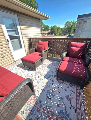 A covered patio area with wicker furniture and red cushions, a patterned rug, and a wooden fence. - Comfy 5 bedroom home conveniently located (St. Catharines)