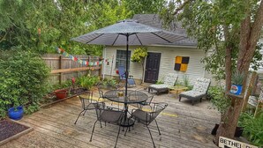 A wooden deck with a metal table and chairs, a covered umbrella, and a small house with a black door and windows. - Towne Motel Camben Room #7 (Camden)