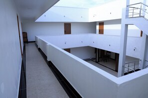 Un interior moderno con un largo pasillo, paredes blancas y un entresuelo con una escalera.