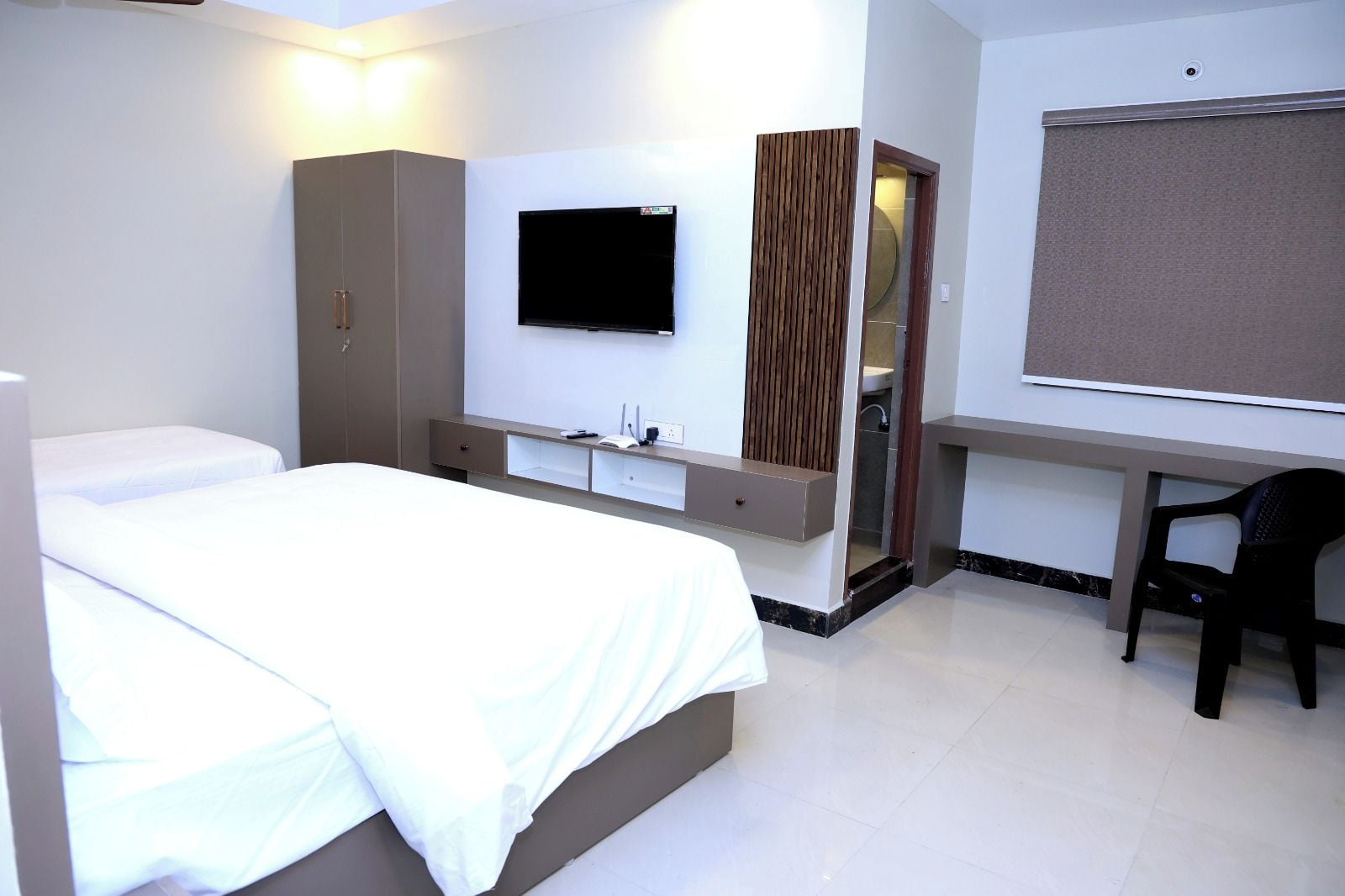 A hotel room with a bed, a desk, a chair, a TV, and a wardrobe.