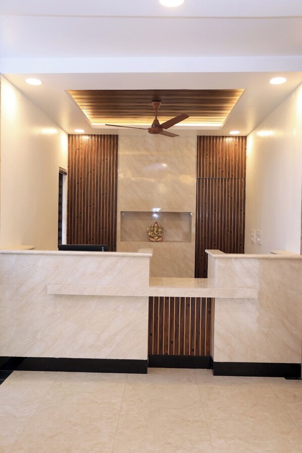 Zona de recepción con diseño moderno, que incluye un mostrador de recepción, un ventilador de techo y un panel decorativo de pared.