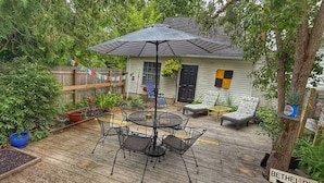 A wooden deck with a metal table and chairs, a covered umbrella, and a small house with a black door and windows. - Towne Motel Camben Room #5 (Camden)