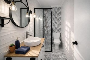 Un baño moderno con un lavamanos redondo, un espejo y una ducha con puerta de cristal.