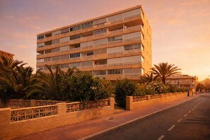 Un hotel de varios pisos con balcones, un paseo pavimentado y palmeras.