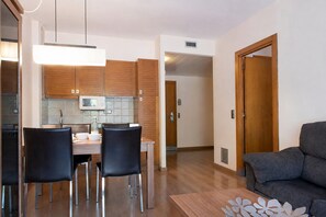 A modern kitchen with wooden cabinets, a dining table with chairs, and a grey sofa in a living area. - Superior Category Apartment in Golf Beach (Pals)