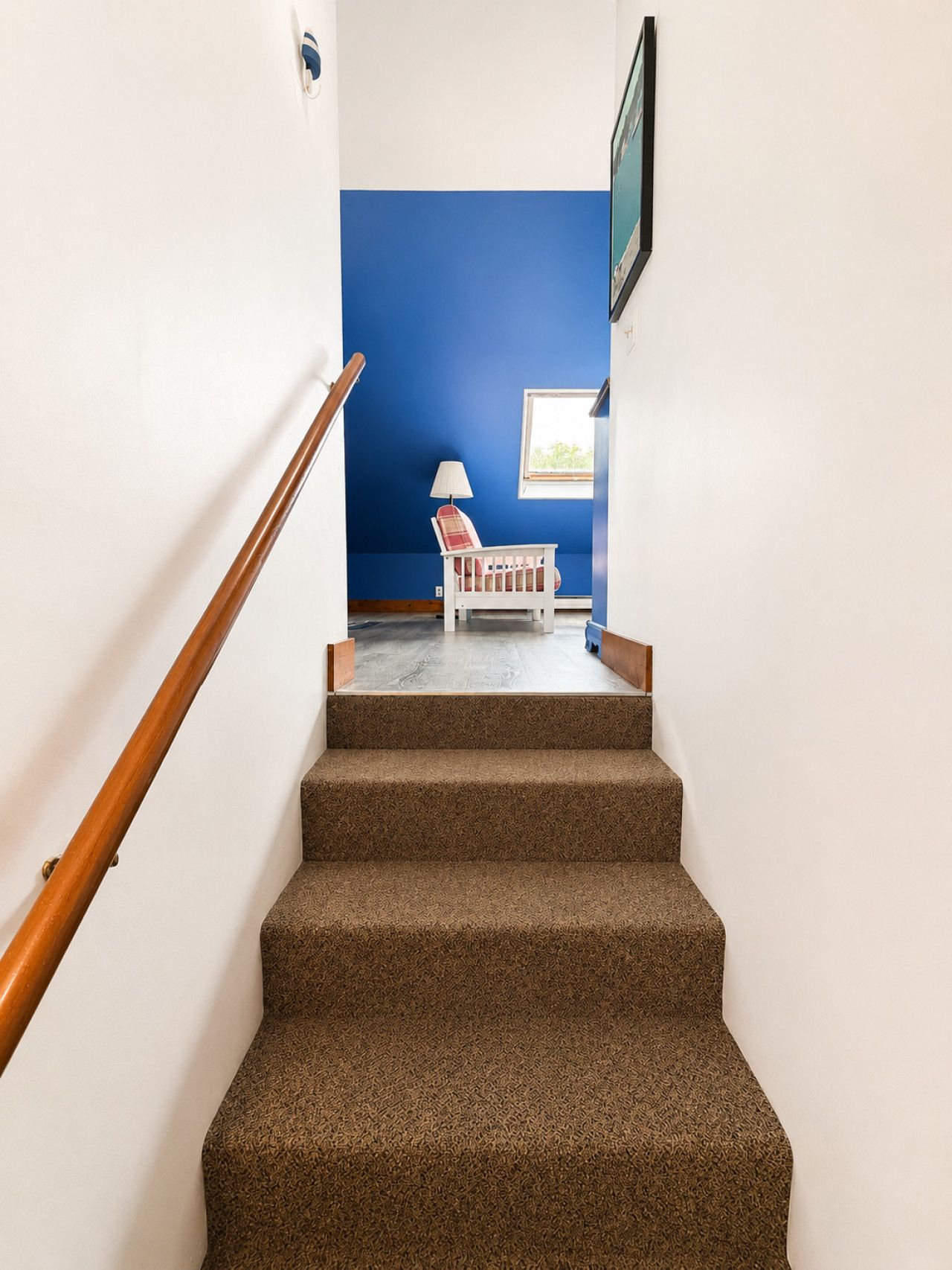 Una escalera con peldaños alfombrados que conduce a una habitación con pared azul y una ventana.
