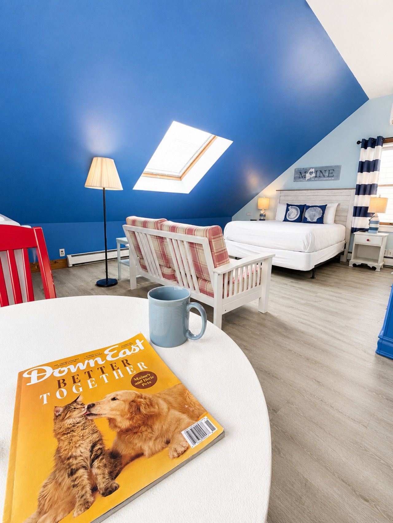 A bedroom with a bed, a chair, a table with a magazine, a lamp, and a window.