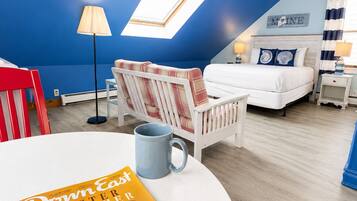 A bedroom with a bed, a chair, a table with a magazine, a lamp, and a window.