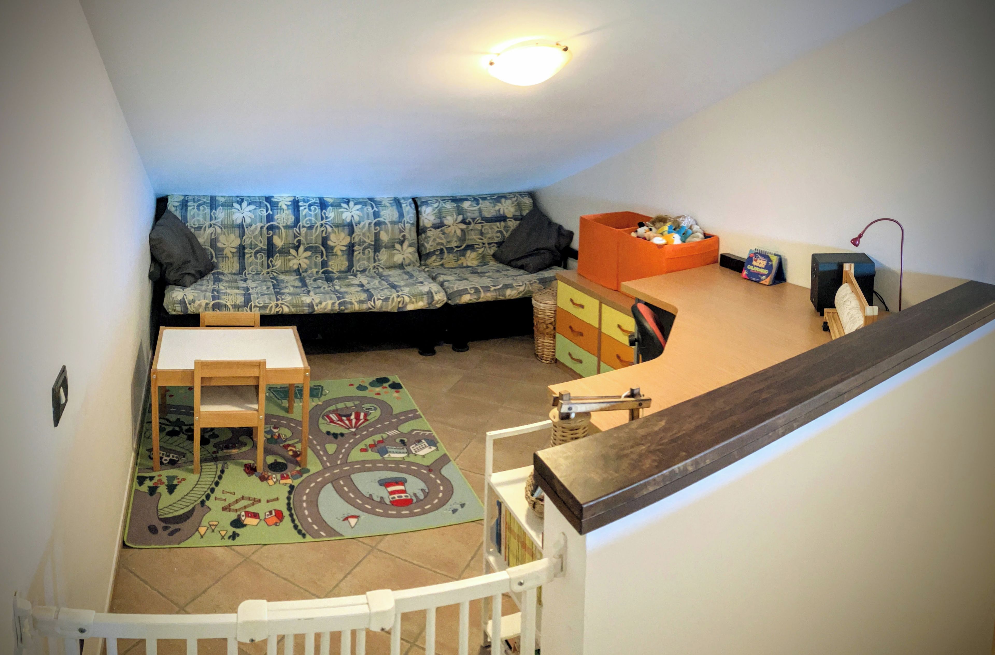 A cozy living space with a sofa, a small table, a play mat, and a storage unit.
