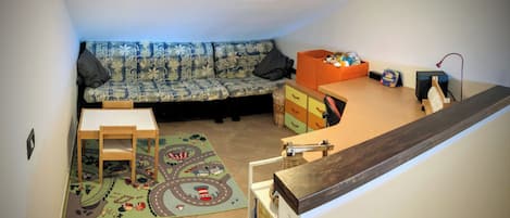 A cozy living space with a sofa, a small table, a play mat, and a storage unit.