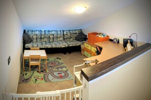 Un espace de vie confortable avec un canapé, une petite table, un tapis de jeu et un meuble de rangement.