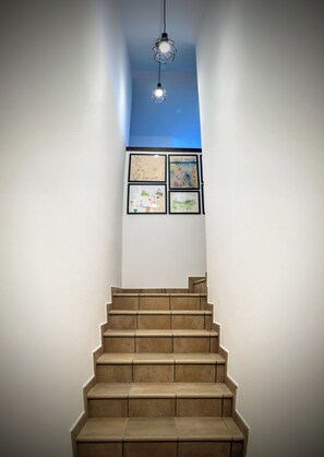 Una escalera con un accesorio de iluminación geométrico arriba y una obra de arte enmarcada en la pared.