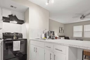 Une cuisine moderne avec des meubles blancs, une cuisinière noire et un évier en acier inoxydable.