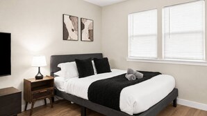 Un dormitorio moderno con cama, mesitas de noche, lámpara, obras de arte y ventana.
