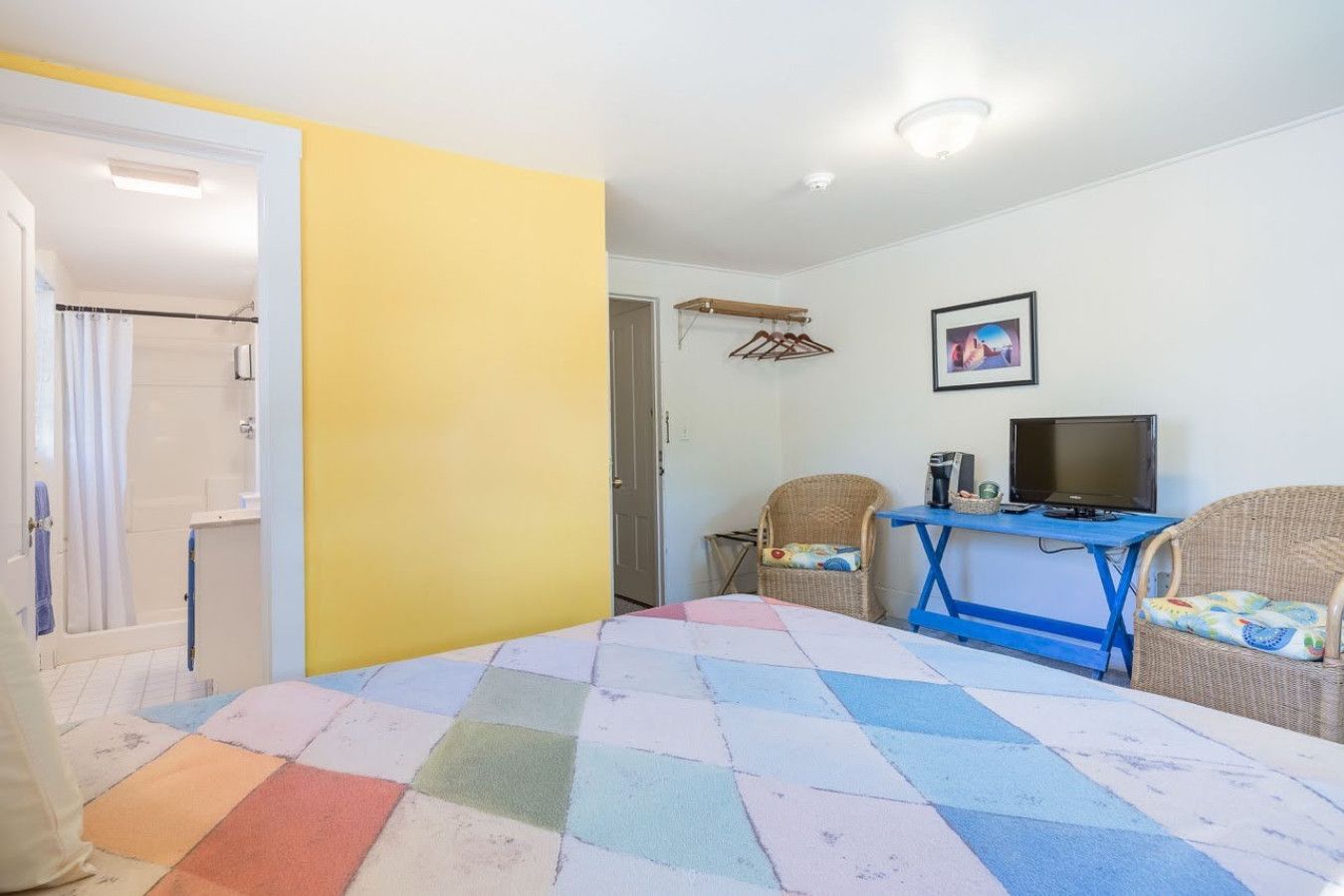 Ein Zimmer mit einem Bett, einem Schreibtisch, zwei Korbstühlen, einem Fernseher und einer Tür zu einem Badezimmer.