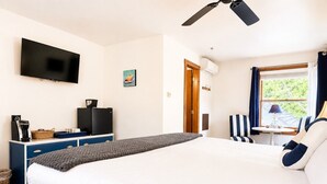 Ein Hotelzimmer mit einem großen Bett, einem Flachbildfernseher, einem Schreibtisch mit Stuhl und einem Fenster mit Vorhängen.