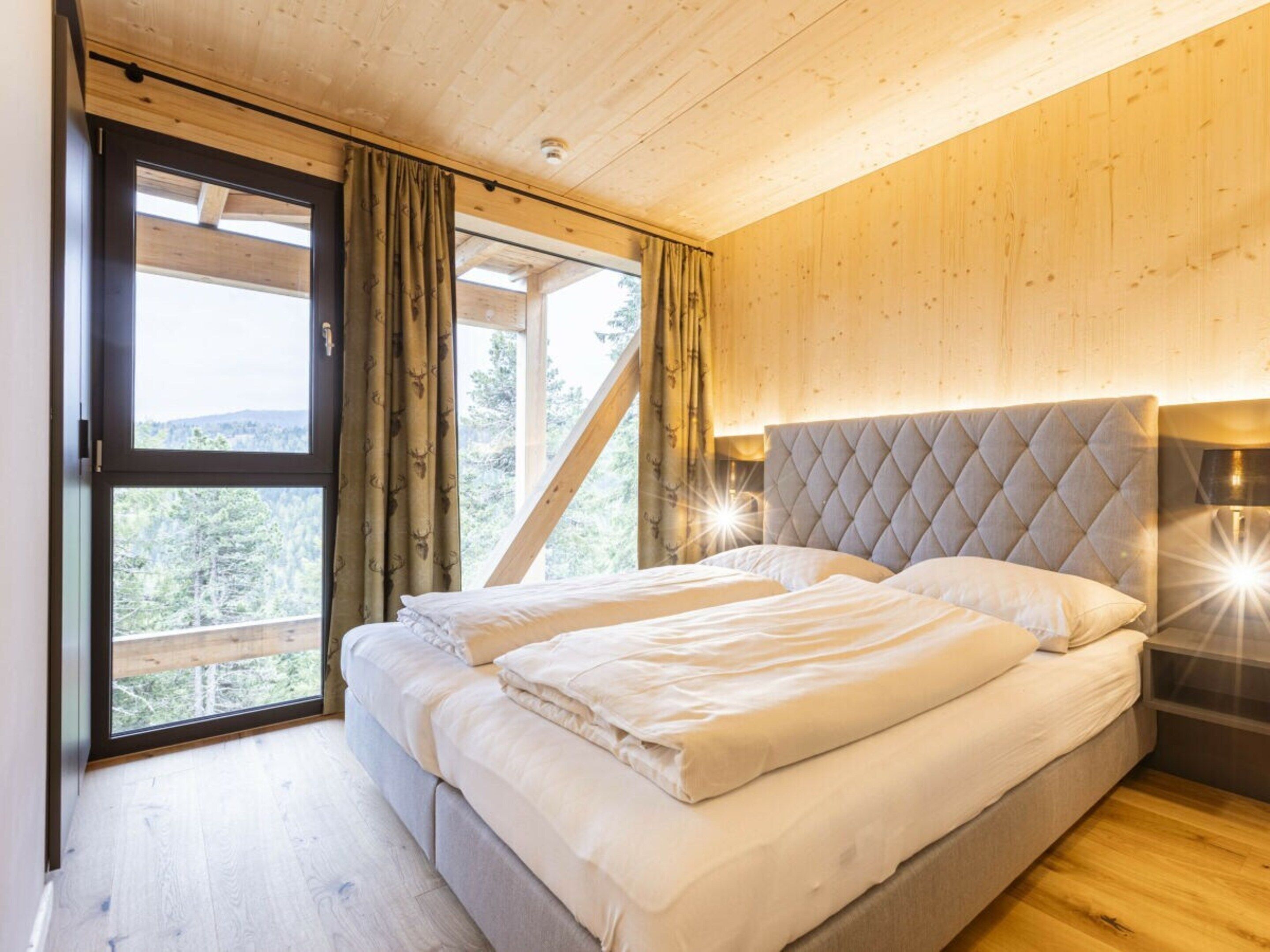 Une chambre à coucher avec un lit, des murs en bois, une fenêtre avec des rideaux et une vue sur les arbres.
