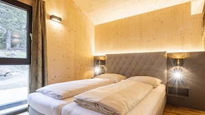A double bed with a headboard, two bedside lamps, and a window with curtains. - Superior Chalet #23 With Sauna & Hot Tub (Stadl-Predlitz)