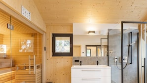 A modern bathroom with a wooden interior, a glass shower enclosure, and a large mirror. - Superior Chalet #23 With Sauna & Hot Tub (Stadl-Predlitz)