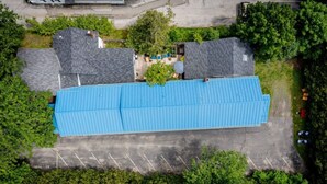 A large building with a blue roof, surrounded by trees and a parking lot. - Towne Motel Camben Room #16 (Camden)