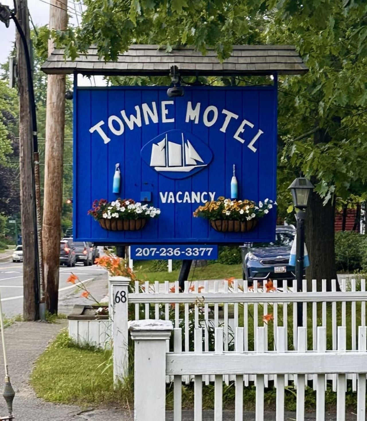 Une enseigne bleue pour le motel Towne, ornée du logo d’un voilier, indiquant qu’il y a des chambres disponibles. Un numéro de téléphone est affiché en dessous.