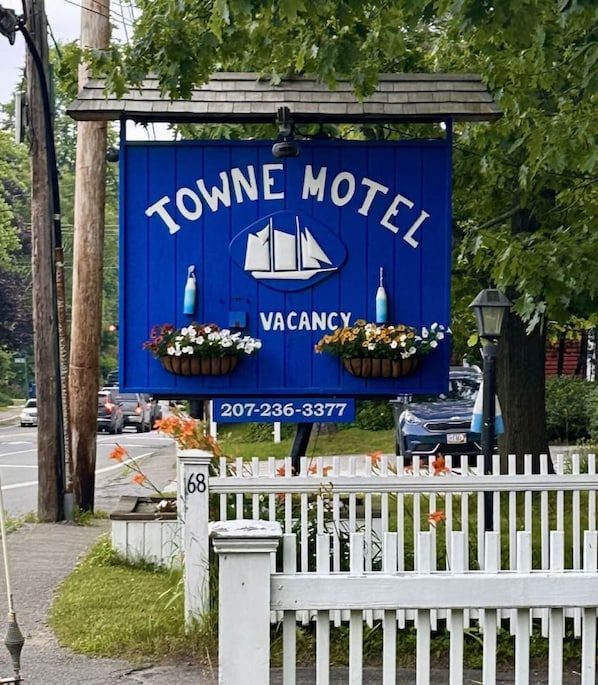 Un senyal blau del Towne Motel amb el logo d'una embarcació de vela, que indica disponibilitat. Hi ha un número de contacte mostrat a sota.