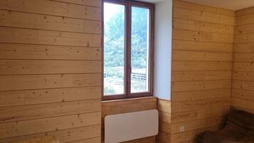 Een kamer met houten wanden, een raam met uitzicht op een bos, een radiator en een bruine bank.