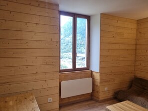 Een kamer met houten wanden, een raam met uitzicht op een bos, een radiator en een bruine bank.