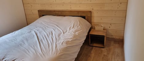 Yhden hengen sänky, jossa on puinen pääty, huoneessa, jonka seinät ja lattia ovat puuta.