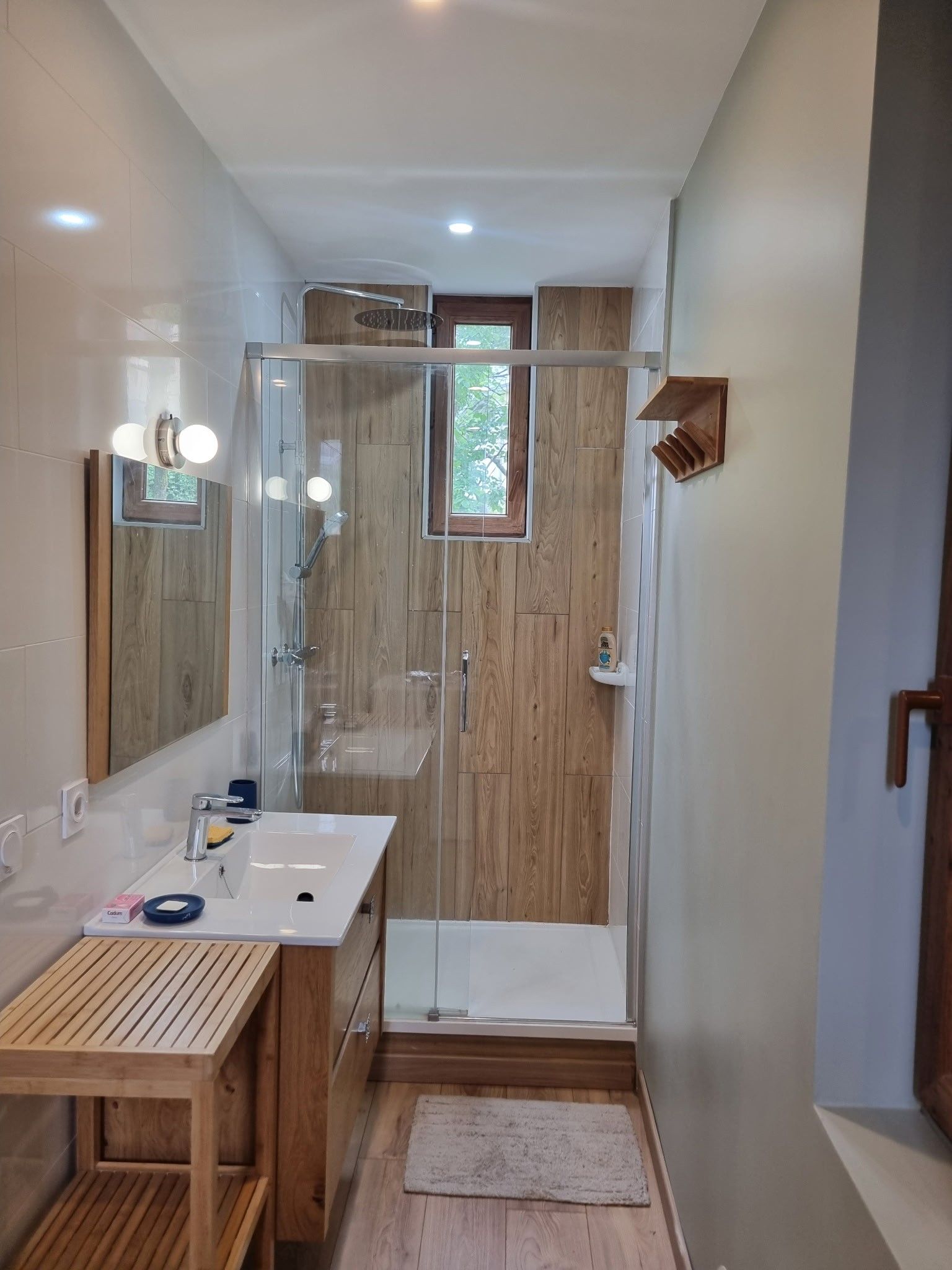 A modern bathroom with a glass shower enclosure, a wooden vanity, and a mirror with lights.