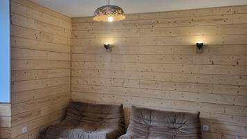 Habitación con paneles de madera, dos zonas de estar con cojines, una mesa de centro de madera y una lámpara colgante.