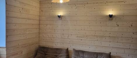 Habitación con paneles de madera, dos zonas de estar con cojines, una mesa de centro de madera y una lámpara colgante.