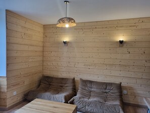 A room with wooden panel walls, two cushioned seating areas, a wooden coffee table, and a hanging light fixture.