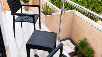 A balcony with a glass railing, two black chairs, a small table, and potted plants.