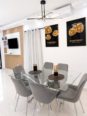 Un comedor moderno con una mesa de vidrio, sillas tapizadas de color gris y un televisor de pantalla plana montado en la pared.