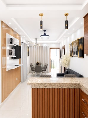 Una cocina moderna con una isla central, iluminación colgante y un comedor con mesa y sillas.