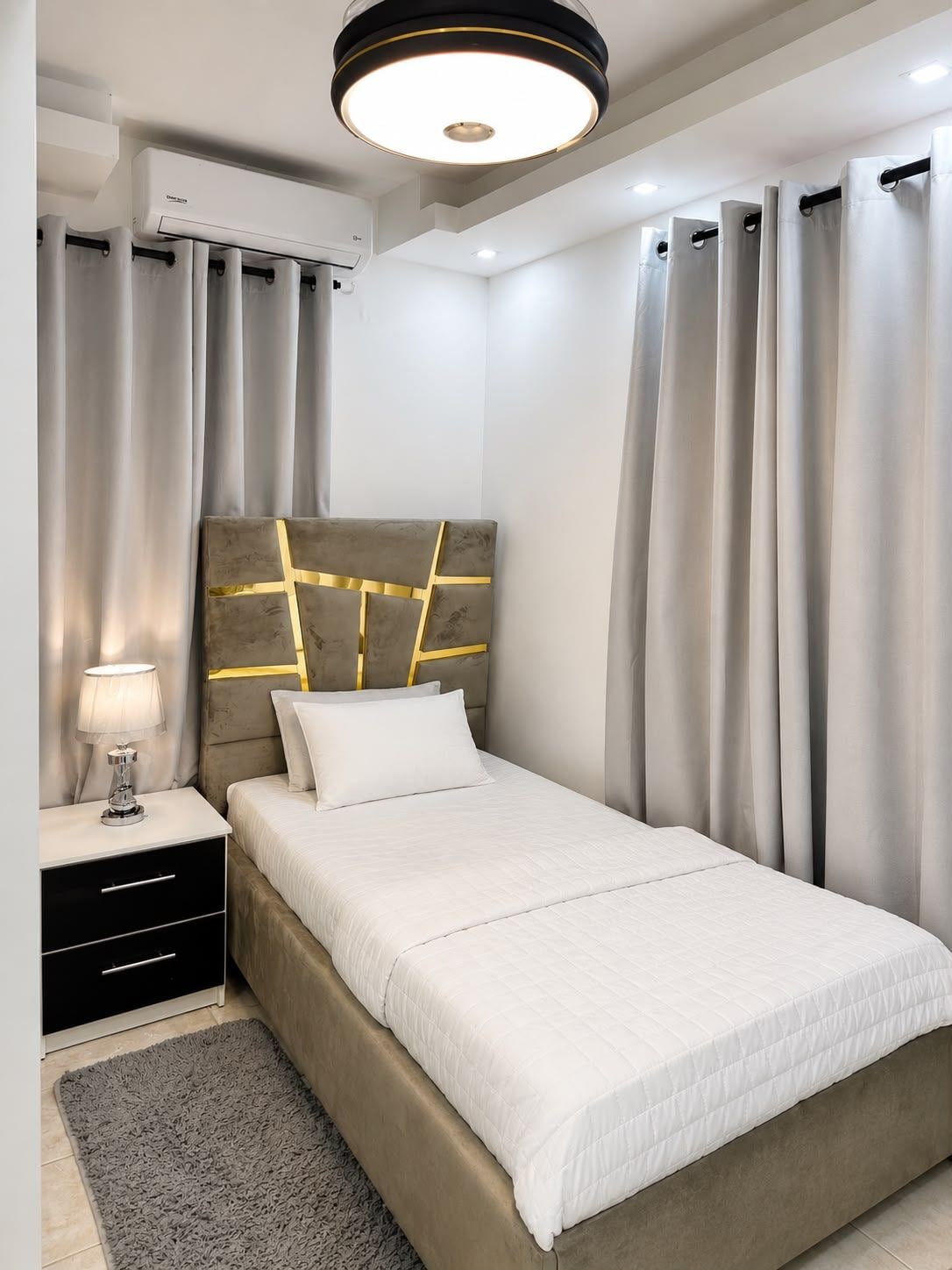 Une chambre à coucher moderne avec un lit, une table de chevet, une lampe et des rideaux.