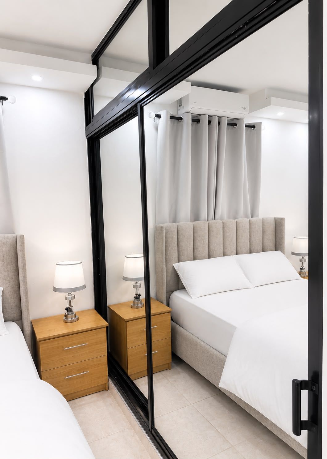 Quarto de hotel moderno com cama, mesas de cabeceira e um espelho grande.