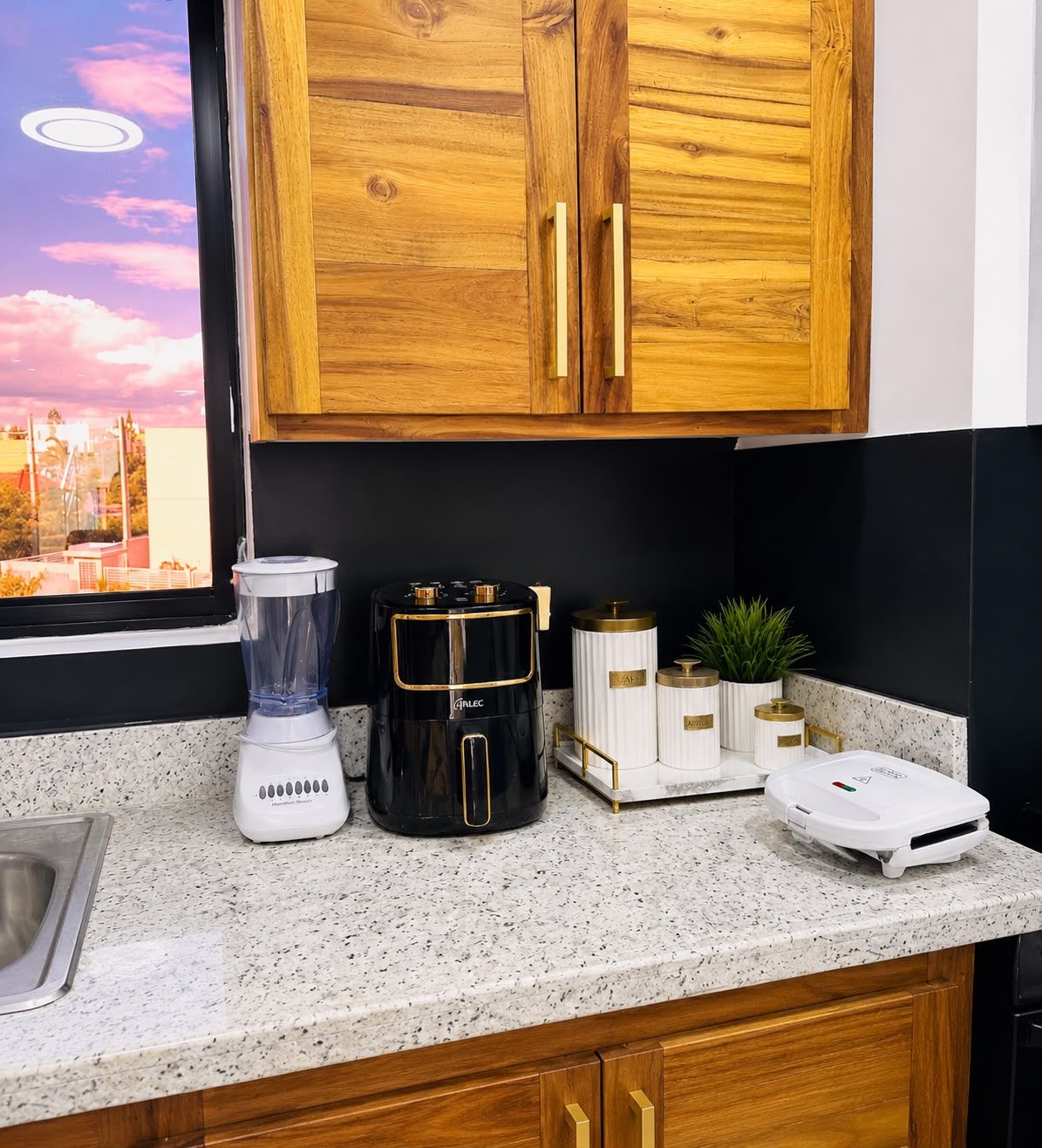 Una cocina con encimera de granito, licuadora, cafetera y balanza.