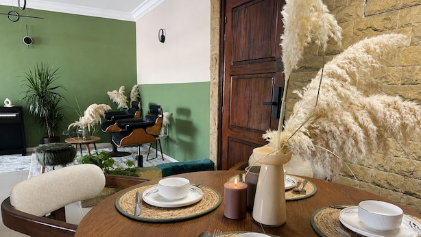 Un comedor con una mesa redonda dispuesta para cuatro personas, una zona de bar con una silla, y una pared verde con una puerta.