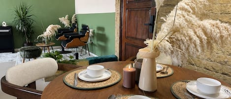 A dining area with a round table set for four, a bar area with a chair, and a green wall with a door.