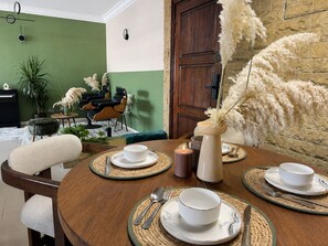 Un comedor con una mesa redonda dispuesta para cuatro personas, una zona de bar con una silla, y una pared verde con una puerta.