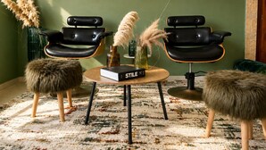 A room with two black leather chairs, a round wooden table with a book titled 'STYLE', and two furry ottomans. - The Olive Flat (Rabat)