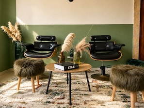 Una habitación con dos sillones de cuero negro, una mesa redonda de madera con un libro titulado 'STYLE' y dos otomanas mullidas.