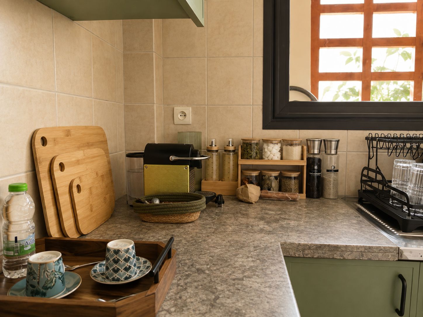 A kitchen with a wooden cutting board, a kettle, and various jars on the counter.