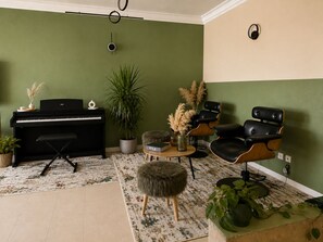 A living room with a piano, chairs, a rug, and a potted plant.