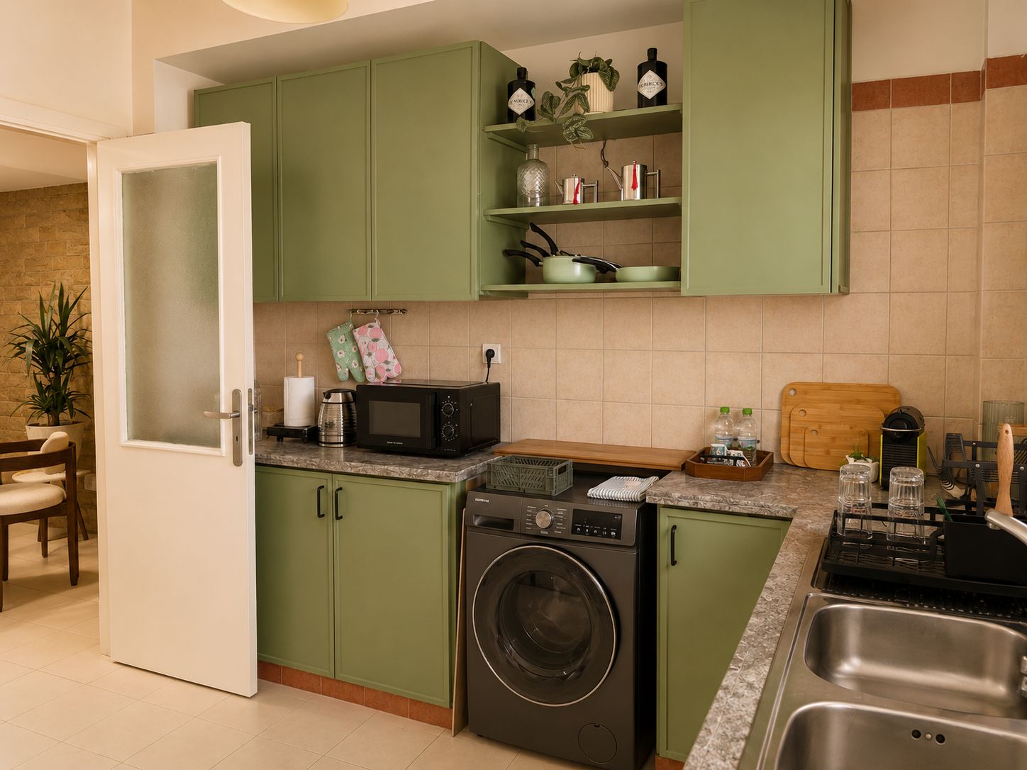 A kitchen with green cabinets, a microwave, a washing machine, and a sink.