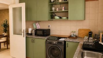 A kitchen with green cabinets, a microwave, a washing machine, and a sink.